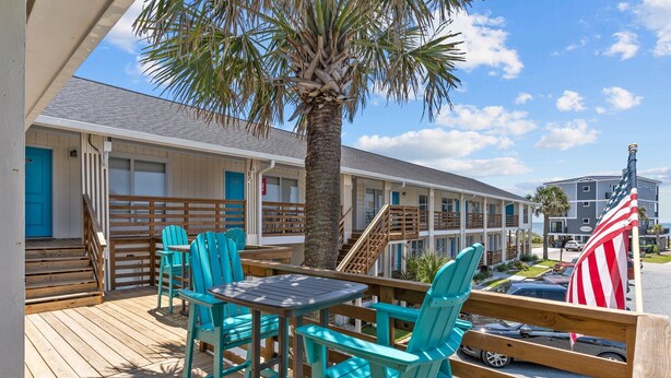 Un motel con terraza de madera, sillas turquesas y una palmera.