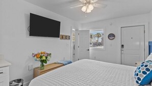 Un dormitorio con cama, ventilador de techo, televisor, puerta y ventana.