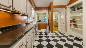 A kitchen with a black and white checkered floor, white cabinets, and a metal trash can.