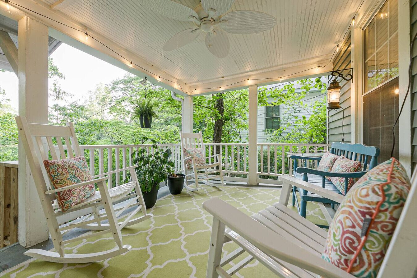 Eine überdachte Veranda mit Schaukelstühlen, einem Tisch und Lichterketten.