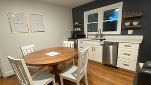 A modern kitchen with white cabinetry, a wooden dining table, and two framed signs on the wall. - mi casa es TU casa (EAST) (Upland)