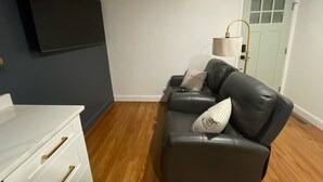 A modern living room with a black leather sofa, a white dresser, and a flat-screen TV mounted on the wall. - mi casa es TU casa (EAST) (Upland)