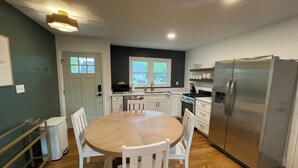 A modern kitchen with white cabinetry, a stainless steel refrigerator, and a round wooden dining table with chairs. - mi casa es TU casa (Center) (Upland)