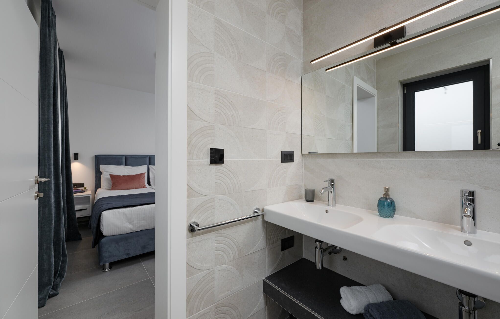 A modern hotel bathroom with a large mirror, two sinks, and a towel rack.