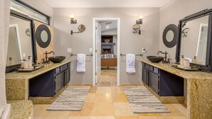 Un baño moderno con dos lavamanos, espejos amplios y una puerta central que da a un pasillo.