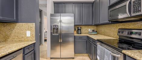 A modern kitchen with granite countertops, stainless steel appliances, and dark cabinetry.