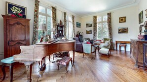 Ein geräumiges Zimmer mit einem Holz-Klavier, einem Kamin und einem großen Fenster mit Vorhängen.