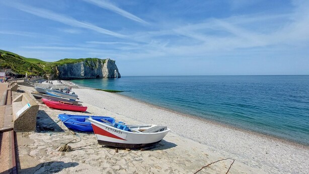 Ein Strand mit an der Küste liegenden Booten, eine Klippe mit einem Höhleneingang und ein klarer, blauer Himmel.