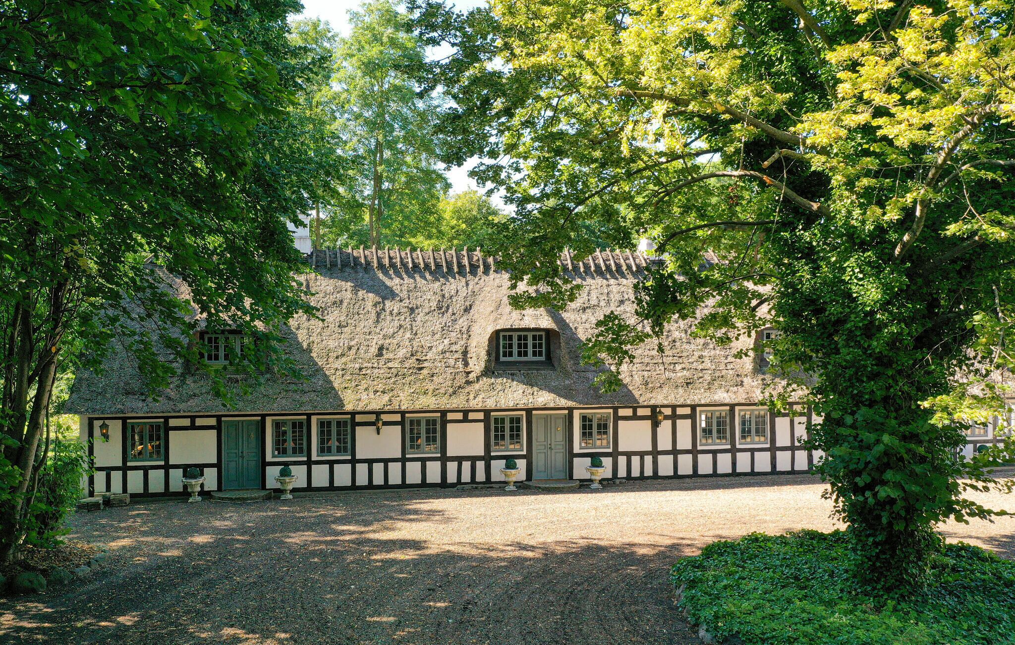A traditional half-timbered house with a stone wall and a gravel driveway.