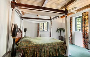 A four-poster canopy bed with a green patterned bedspread, a potted plant, and a view of the outdoors through a window. - Beautiful home in Nørre Aaby with sauna (Nørre Aaby)
