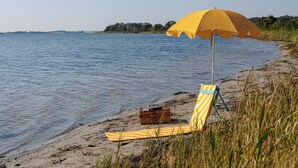 Une chaise de plage avec une serviette à rayures et un parasol jaune à pois, sur une plage de sable.