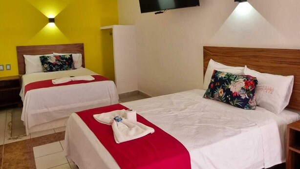 Habitación de hotel con dos camas, un televisor montado en la pared y una pared de acento roja.