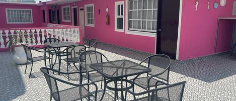 A pink building with a tiled patio, outdoor seating, and a door marked with the number 201.