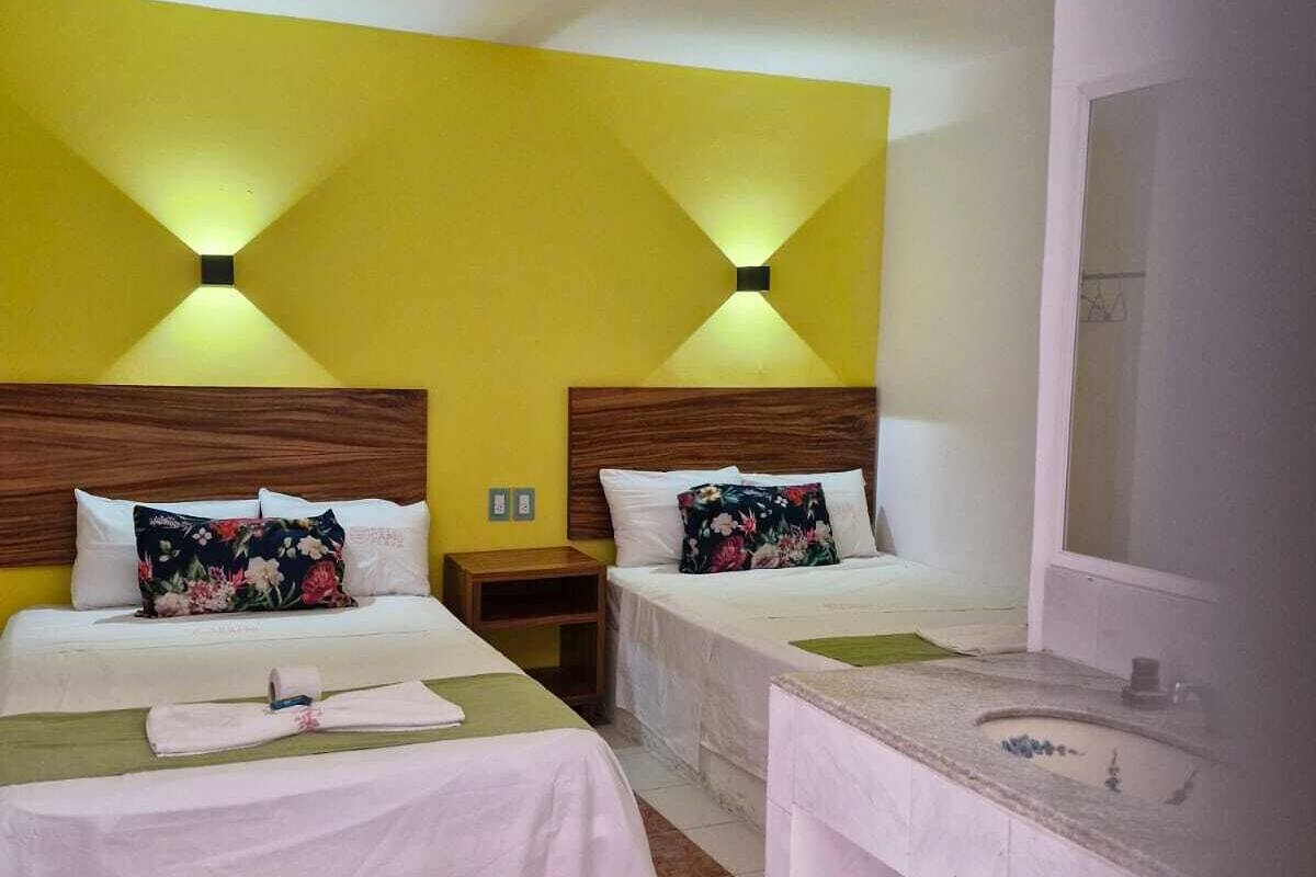 A hotel room with two beds, a bathroom with a sink, and a mirror.