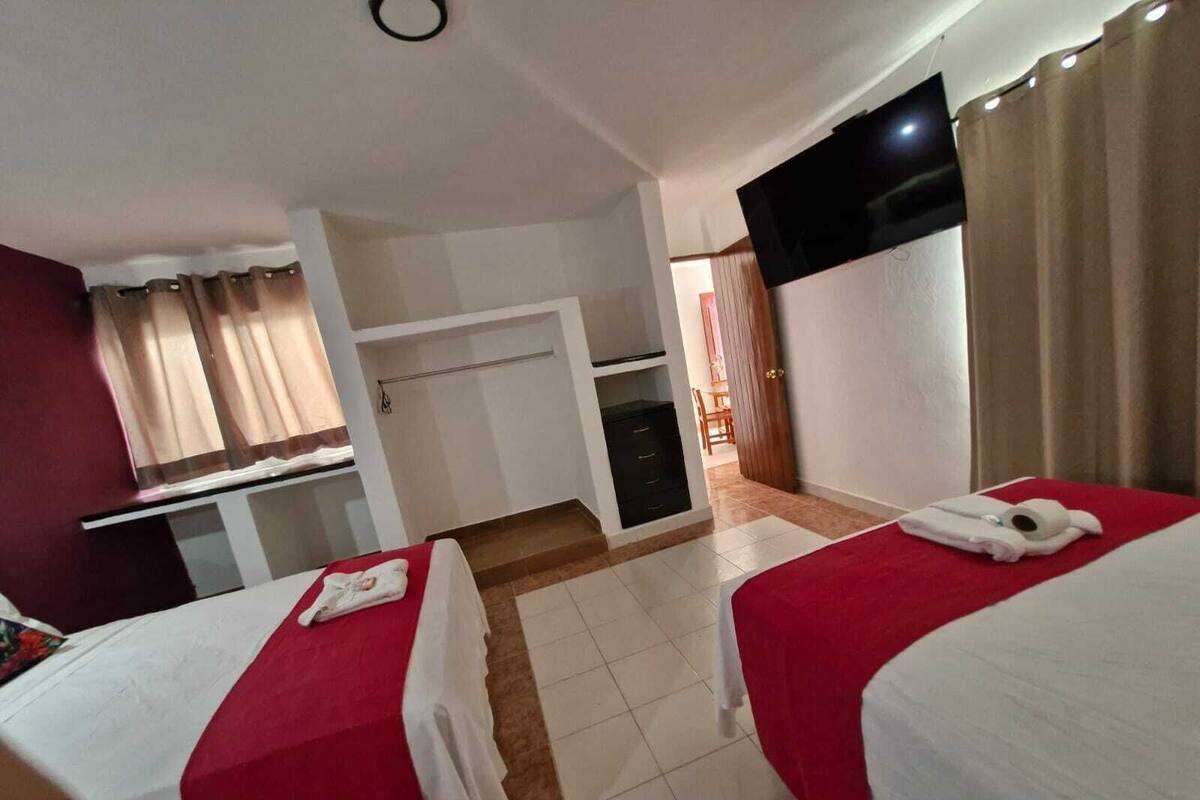 A hotel room with two beds, a TV, a desk, and a bathroom visible through an open door.
