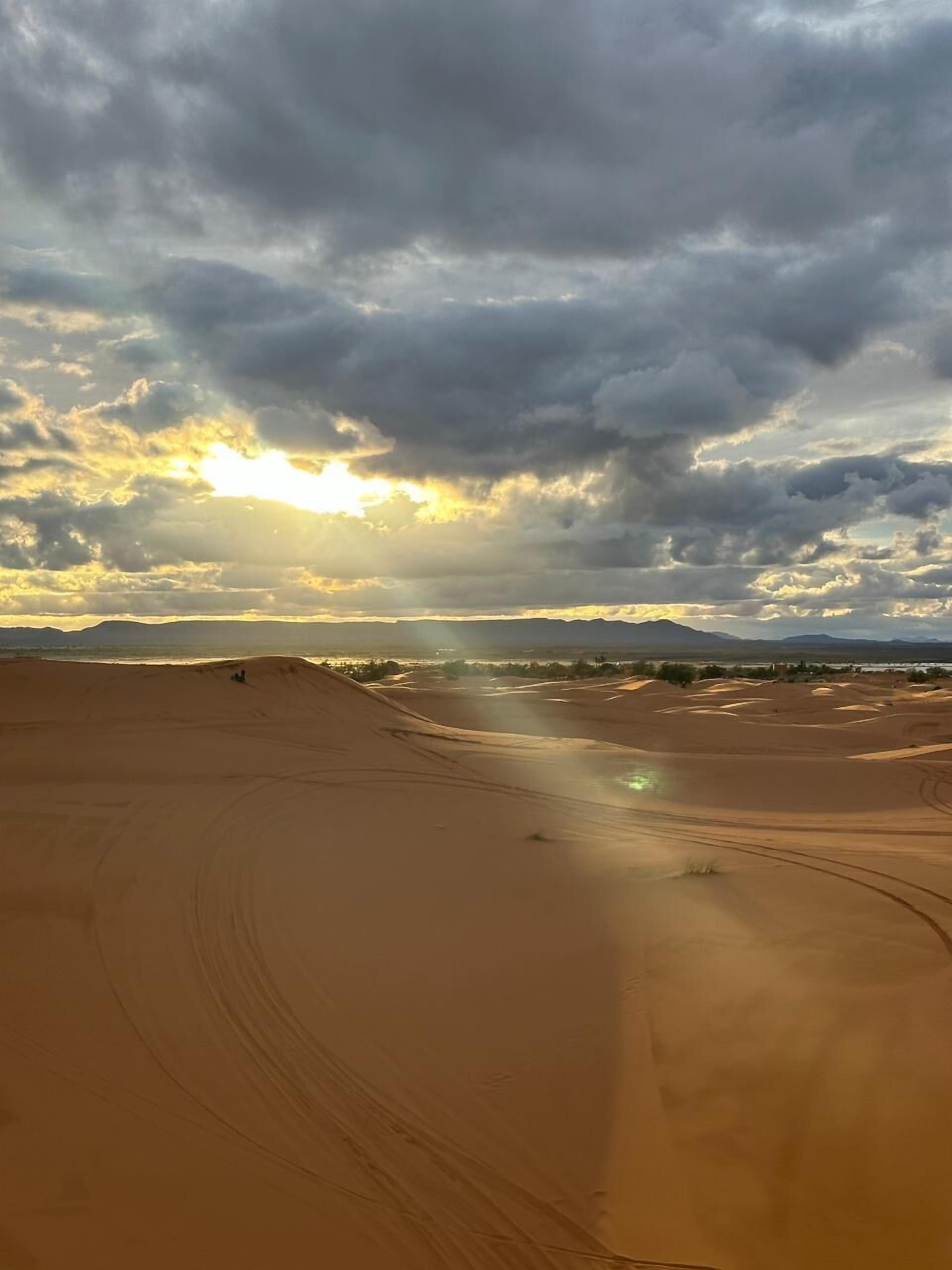 A desert landscape with sand dunes and a cloudy sky.