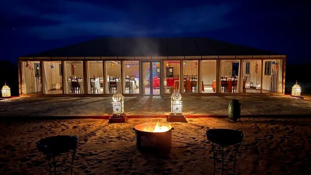 Ein Gebäude mit Glasfassade, einem Feuerkorb und zwei Laternen im Sand.