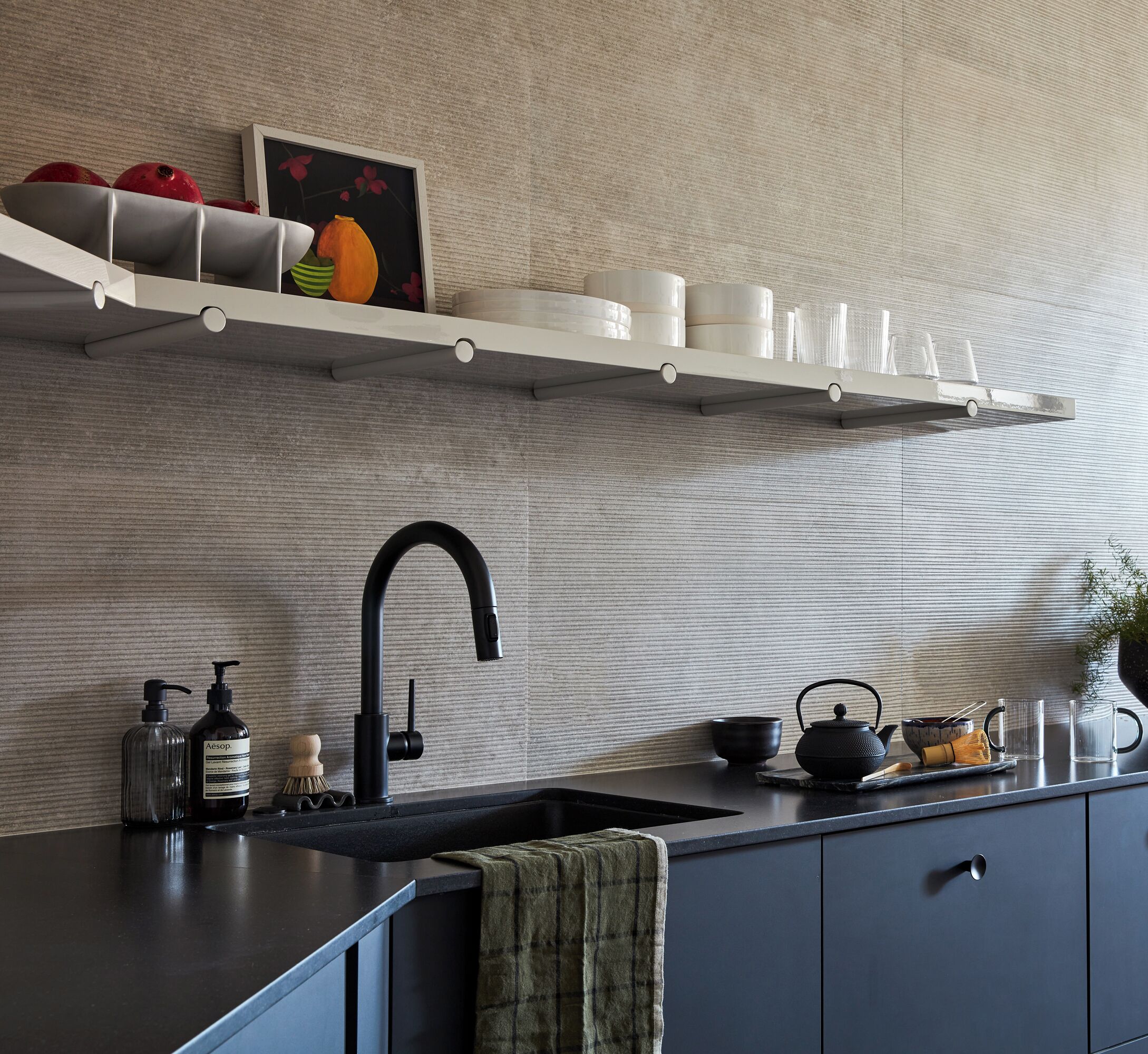 Una cocina moderna con un grifo negro, un fregadero y una encimera con varios objetos, como una botella, un cepillo y un hervidor.