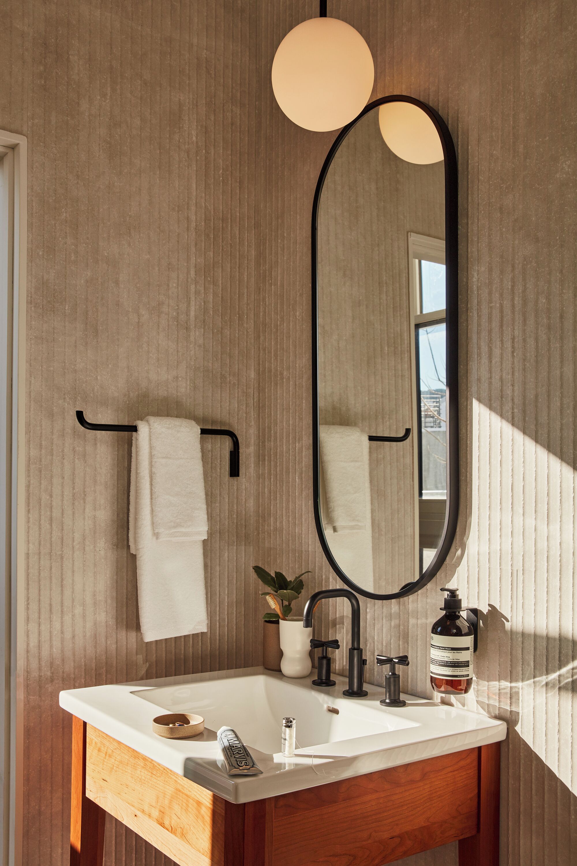 A bathroom with a wooden vanity, a white sink, a black faucet, a round mirror, and a towel rack.