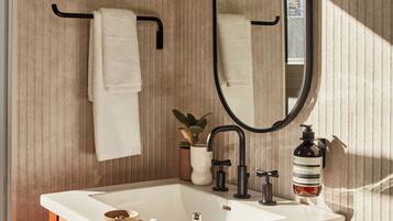 A bathroom with a wooden vanity, a white sink, a black faucet, a round mirror, and a towel rack.