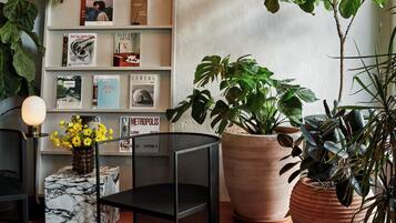 Un coin lecture confortable avec une bibliothèque, de grandes plantes en pot et une table en marbre.