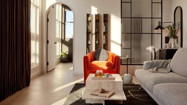 A modern living room with a sofa, a red armchair, a coffee table, and a bookshelf. - Archway Hotel & Residences (Philadelphia)