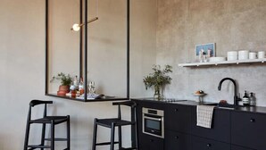 A modern kitchen with a large window, two bar stools, a built-in oven, and a black countertop. - Archway Hotel & Residences (Philadelphia)