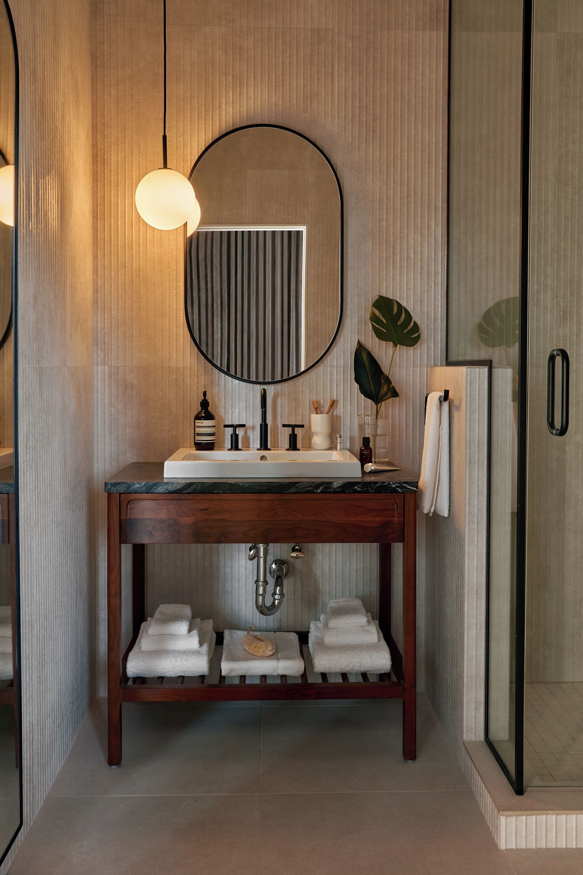 Un baño moderno con tocador de madera, un espejo redondo y una cabina de ducha de vidrio.