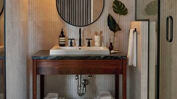 Un baño moderno con tocador de madera, un espejo redondo y una cabina de ducha de vidrio.