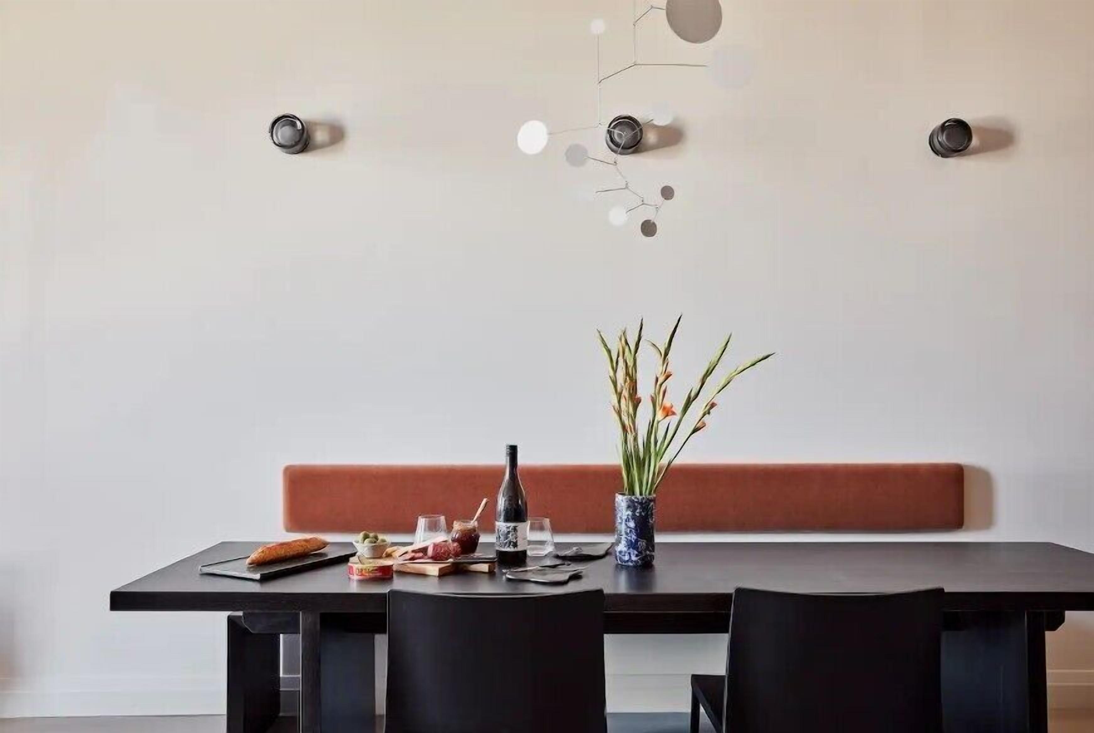 A dining area with a table set for two, a vase with flowers, and a wall-mounted light fixture.
