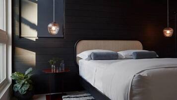 A modern bedroom with a large bed, a small bedside table, a potted plant, and two hanging pendant lights.