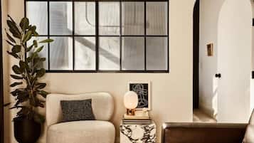 A room with a large window, a potted plant, a sofa, a side table with a lamp, and a framed abstract artwork.