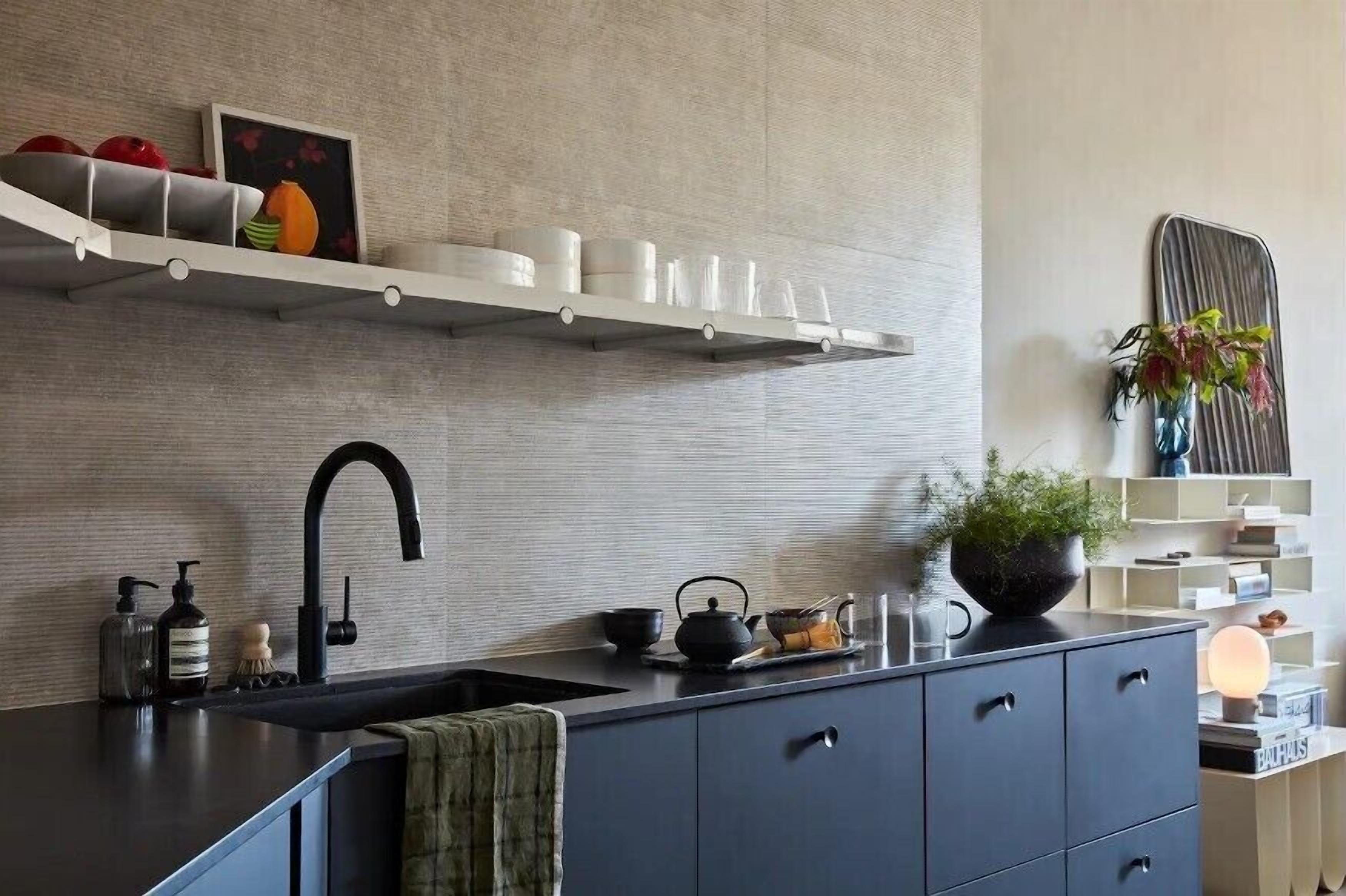 A modern kitchen with a dark countertop, a black faucet, and a white shelf above.