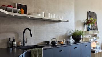 A modern kitchen with a dark countertop, a black faucet, and a white shelf above.