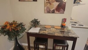Zona pranzo con tavolo in legno, due sedie, un vaso con fiori e dipinti astratti alle pareti.
