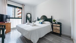 A hotel room with a bed, a TV, a dresser, and a window with curtains.