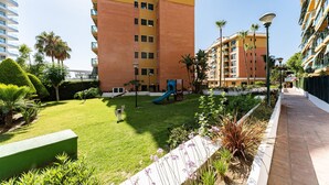 A courtyard with a playground, palm trees, and a building with multiple floors and balconies.