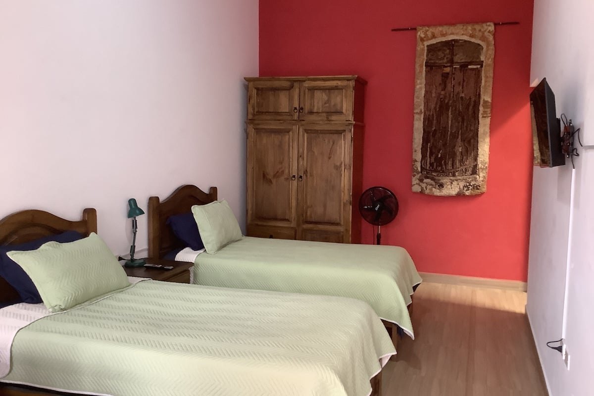 Un dormitorio con dos camas, un armario de madera, un ventilador y una pared roja.