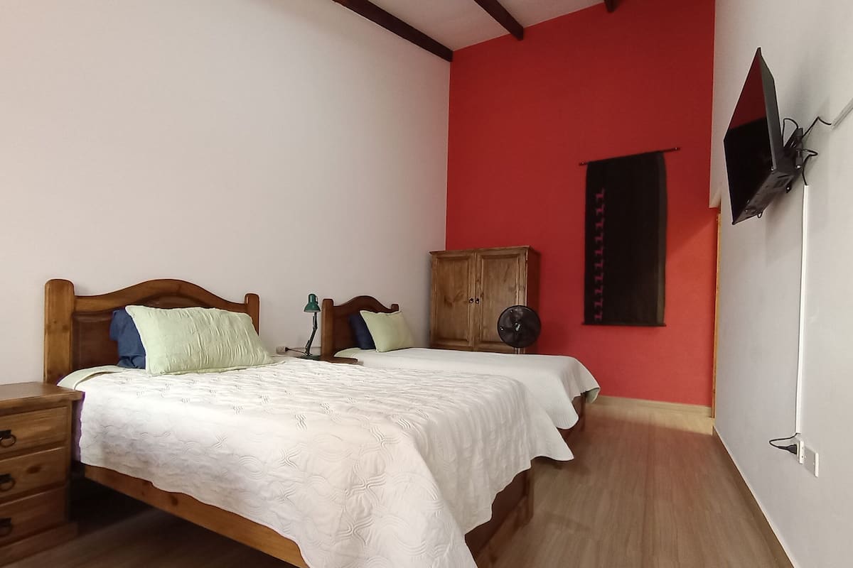 Un dormitorio con dos camas, un armario de madera, un escritorio y un televisor montado en la pared.