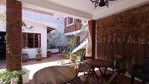 Une vaste terrasse dotée d’une table et de chaises en bois, entourée de plantes en pot et d’un mur en briques.
