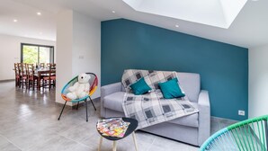 Een moderne woonkamer met een grijze bank, kussens in teal, een geruit plaid en een kleurrijke fauteuil.