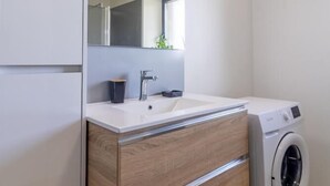 Een moderne badkamer met een witte wastafel, een houten wastafelmeubel, een spiegel en een ingebouwde wasmachine.