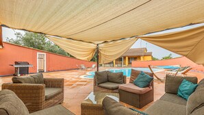 Ein überdachter Außenbereich mit Korbmöbeln und einem Pool im Hintergrund.