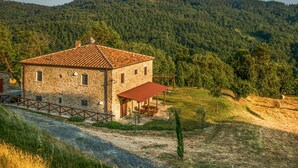 A stone house with a tiled roof, a covered porch, and a view of a forested mountain. - Pet friendly apartment (Ponte alla Piera)