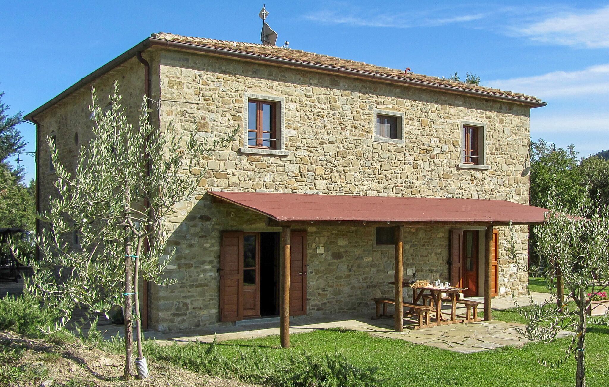 Un edificio de piedra con toldo rojo, un pequeño patio con mesa y sillas, y una puerta.