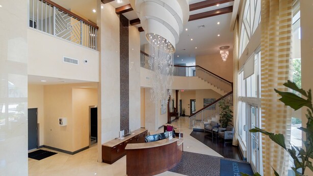 A spacious lobby with a reception desk, a chandelier, and a staircase leading to an upper level.