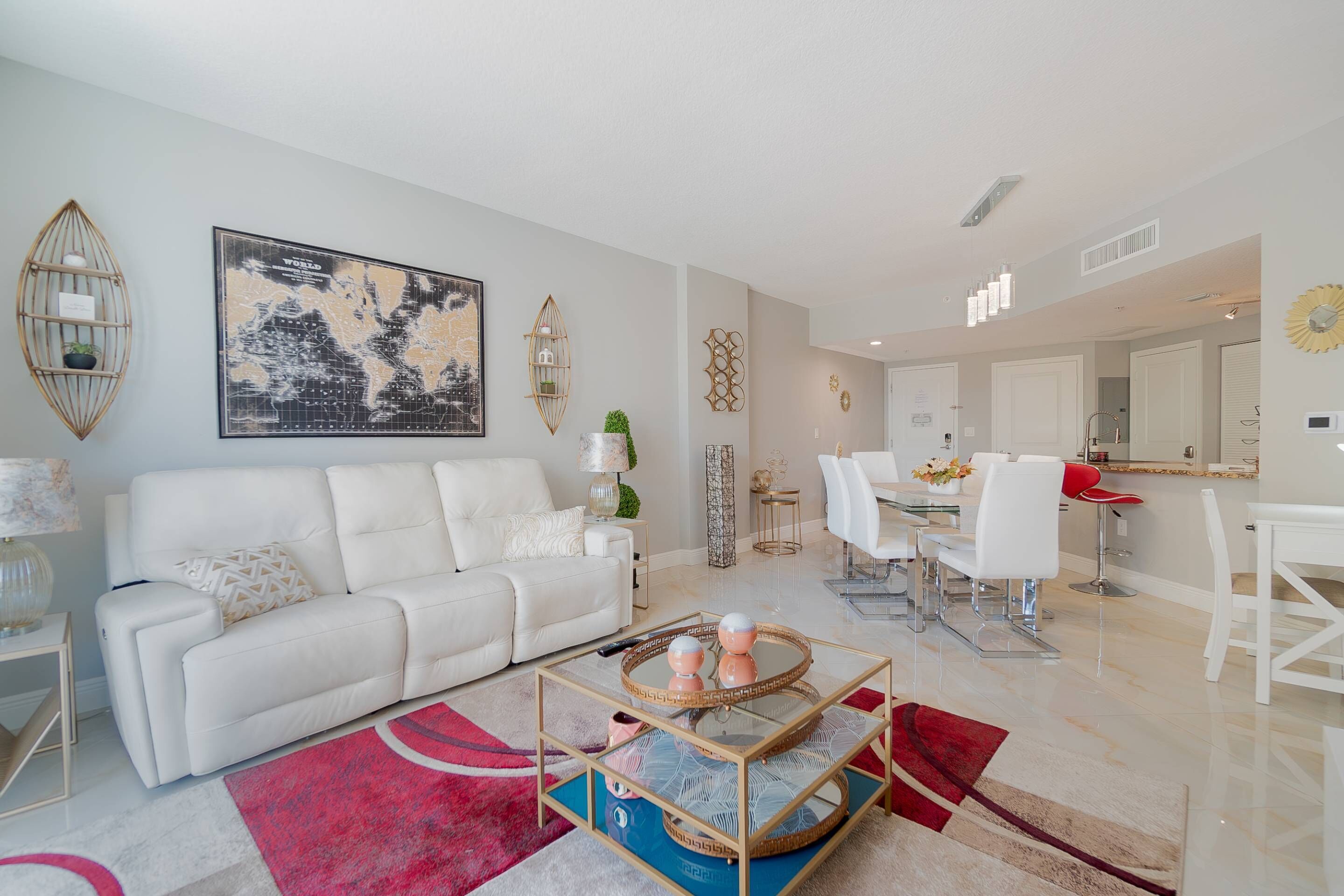 A modern living room with a white sofa, a coffee table, and a dining area with white chairs and a red bar stool.