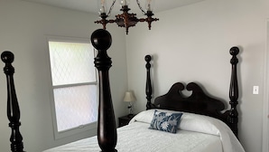 Un dormitorio con cama con dosel, un candelabro y una ventana con persianas.