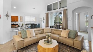 A spacious living room with a beige sectional sofa, a wooden coffee table, and a kitchen area in the background. - Wish Upon A Palm | Private Pool & Resort Amenities (Kissimmee)
