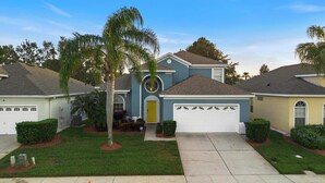 A residential house with a garage, a front yard with a palm tree, and a driveway. - Wish Upon A Palm | Private Pool & Resort Amenities (Kissimmee)